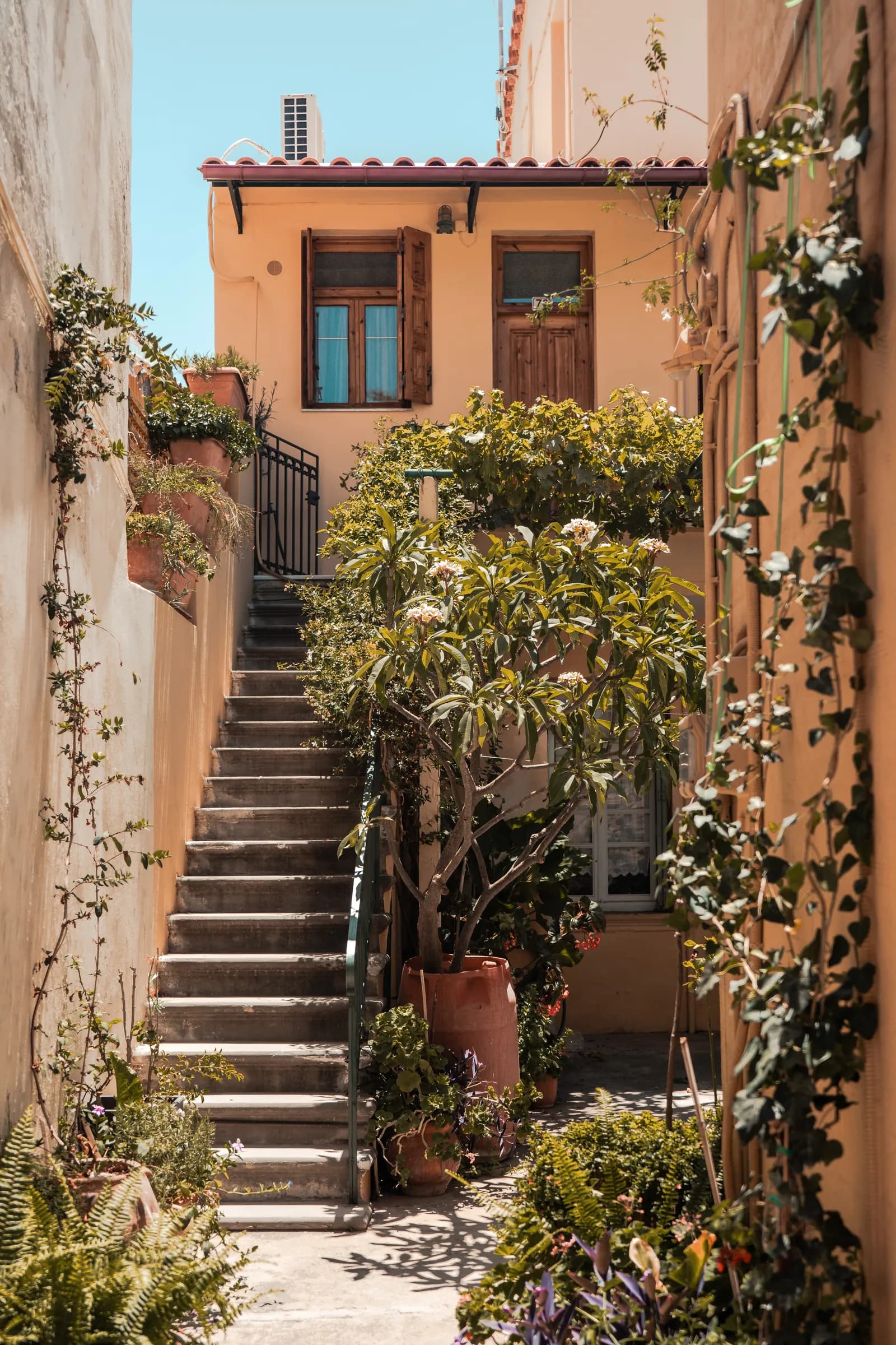 Escalier de pierre et façade ocre envahie de plantes dans une ruelle de la vieille ville de Réthymnon