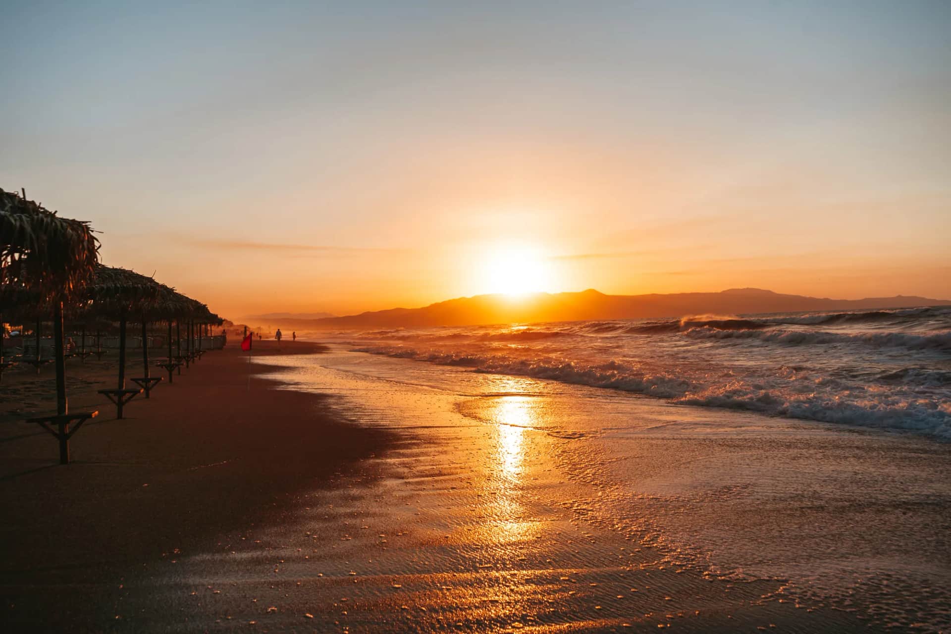 Coucher de soleil sur la plage de Platanias presque vide, ses parasols de paille et les vagues dorées
