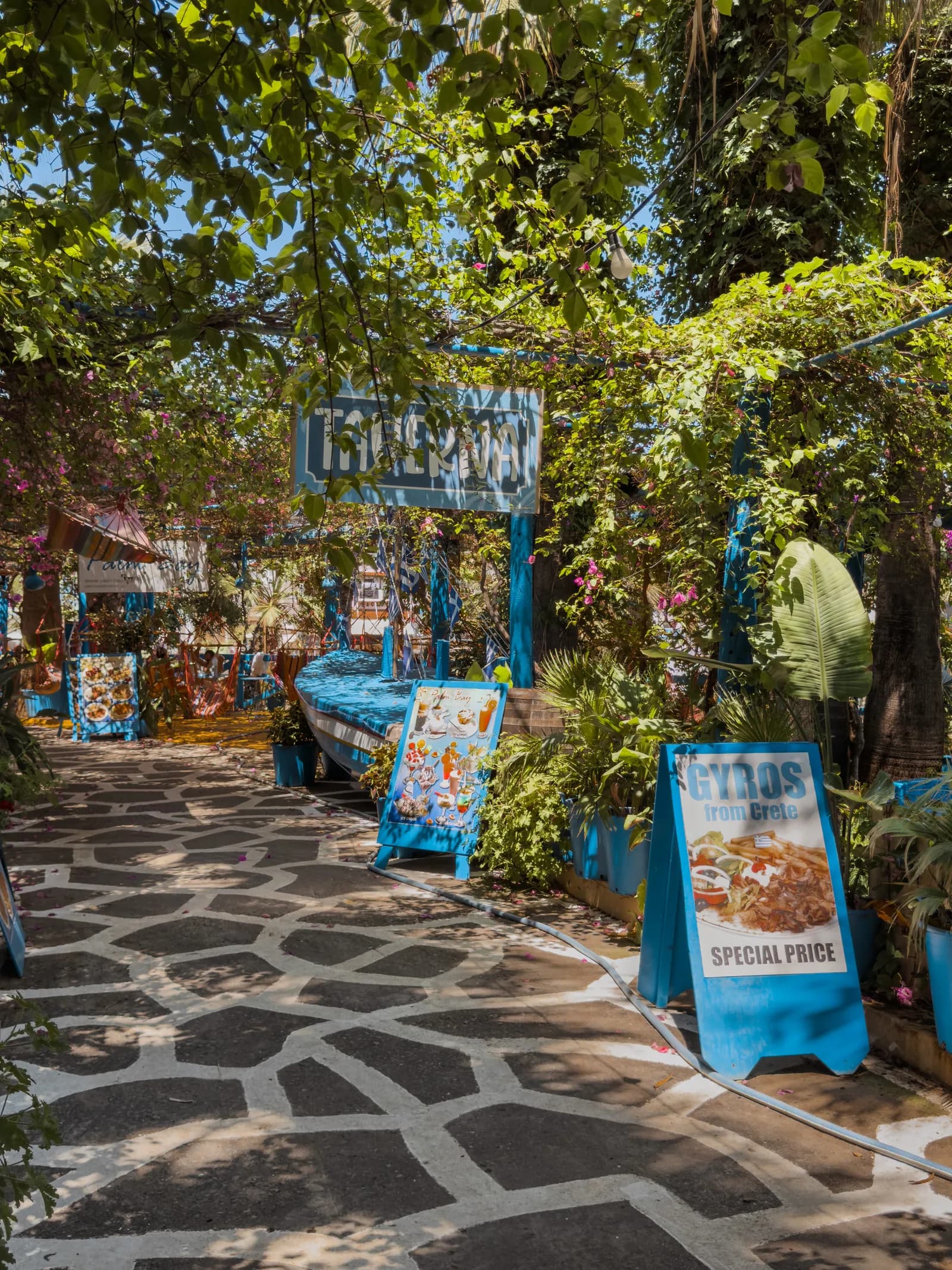 Allée dallée ombragée par la verdure menant aux tavernes du petit port de Sisi