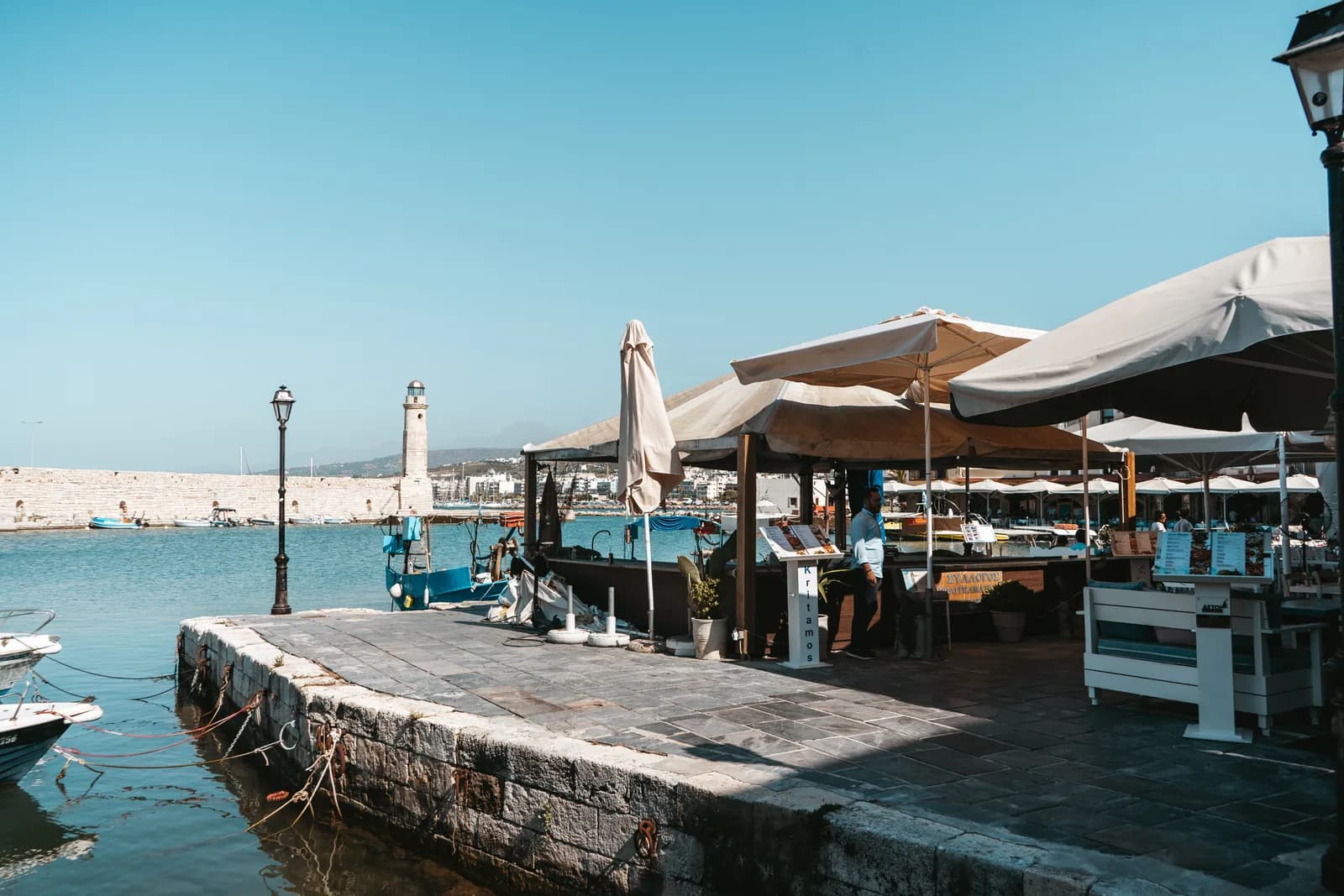 Terrasses de restaurants sous les parasols sur le vieux port vénitien de Réthymnon, face au phare