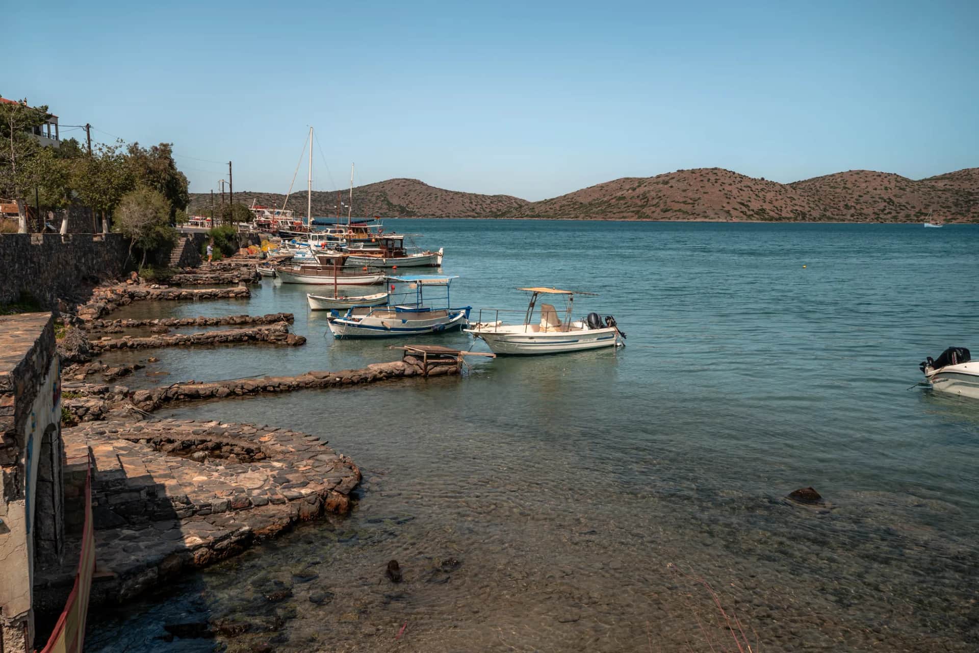 Petits quais de pierre et barques amarrées dans l'eau claire du front de mer d'Elounda, face aux collines