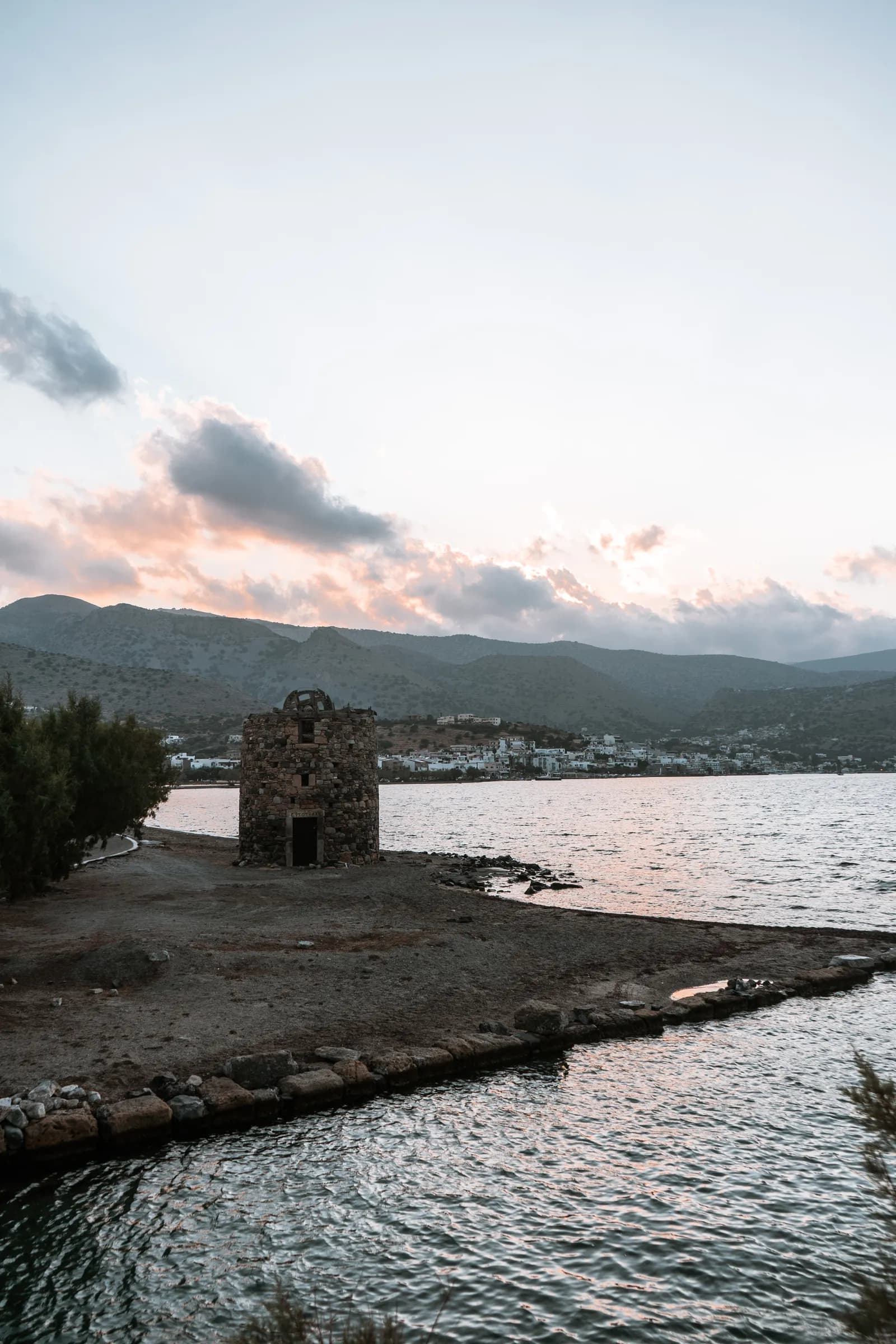 Vieux moulin de pierre au bord de l'eau près de la chaussée, avec Elounda au pied des montagnes au crépuscule