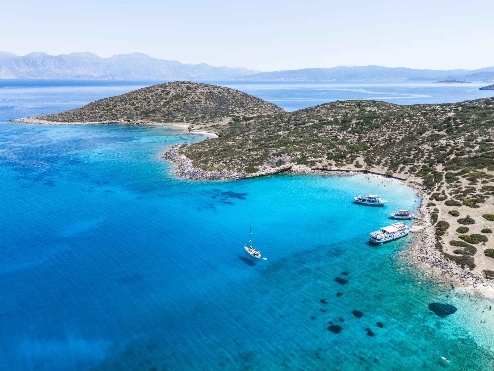 Vue aérienne de la crique de Kolokytha, ses bateaux ancrés dans l'eau turquoise et la garrigue de la péninsule
