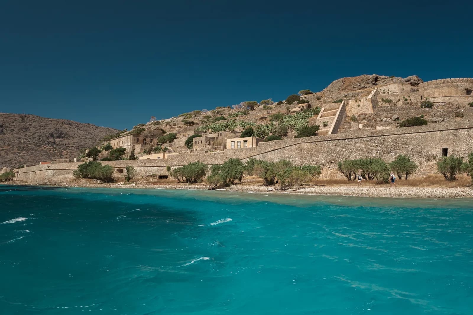 Les remparts vénitiens et les maisons de Spinalonga vus depuis le bateau, au-dessus d'une eau turquoise