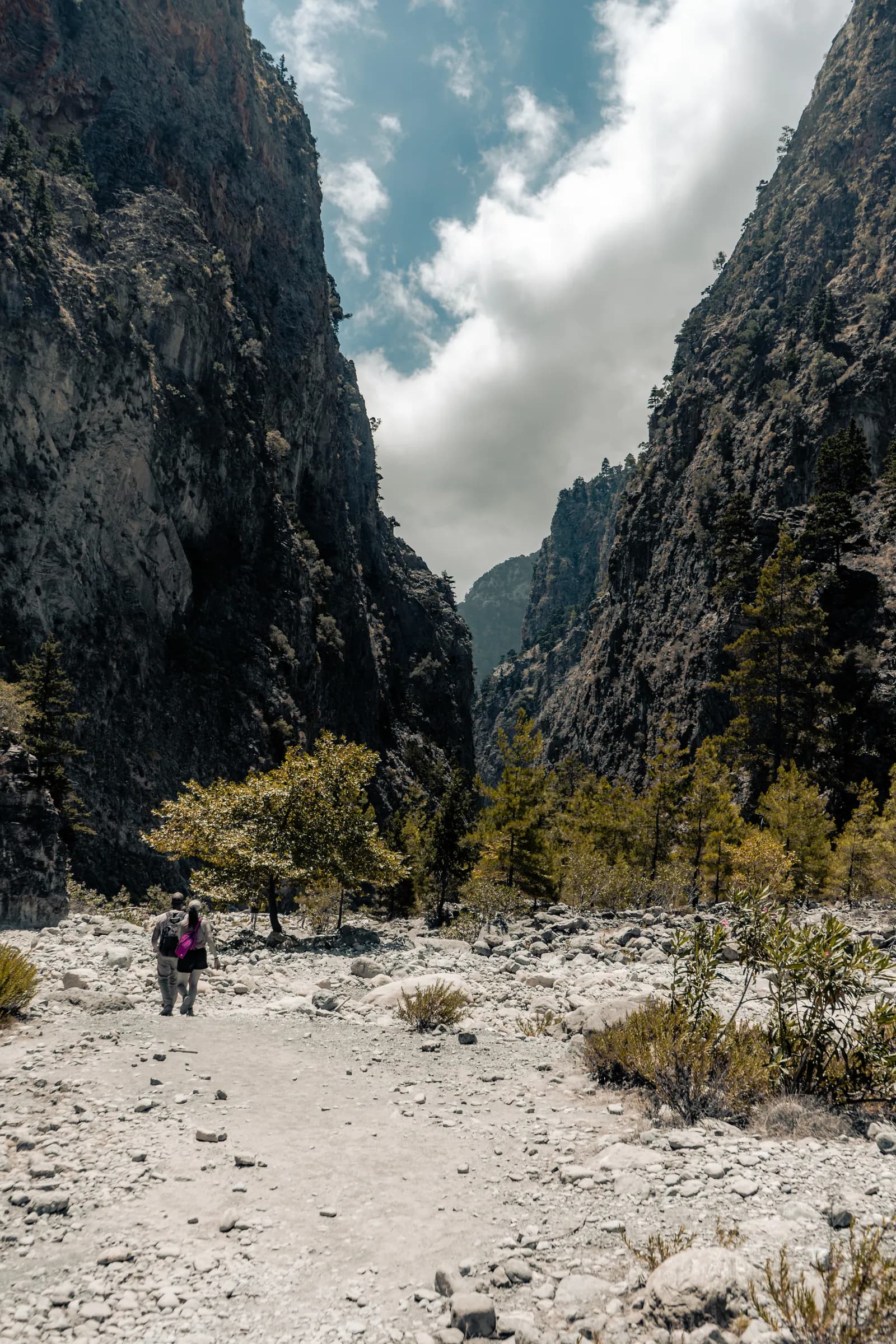 Randonneurs au pied des hautes parois des gorges de Samaria, sur le lit de galets du torrent