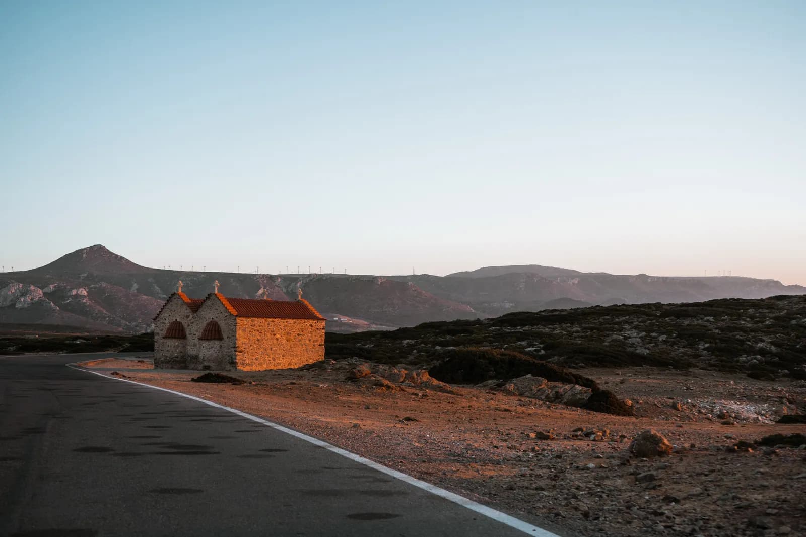 Chapelle de pierre dorée par la lumière du soir au bord d'une route déserte de l'extrême est de la Crète