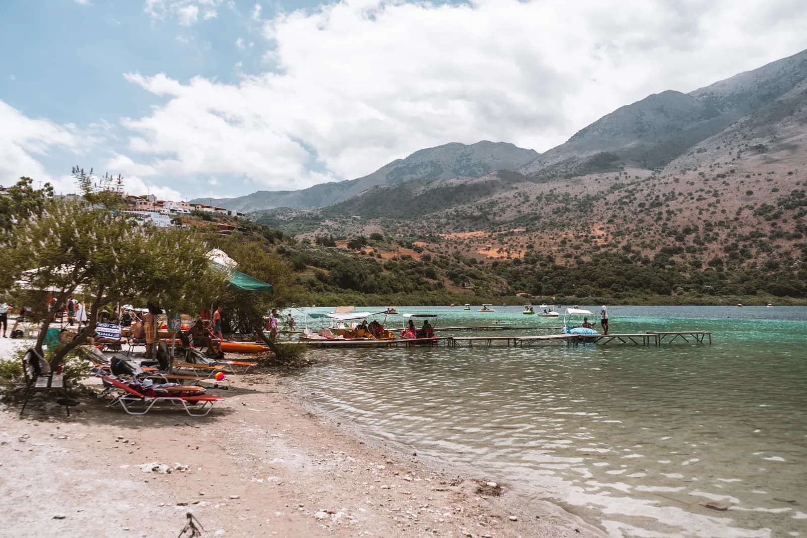Transats et parasols sur la petite plage du lac Kournas, près des pontons à pédalos