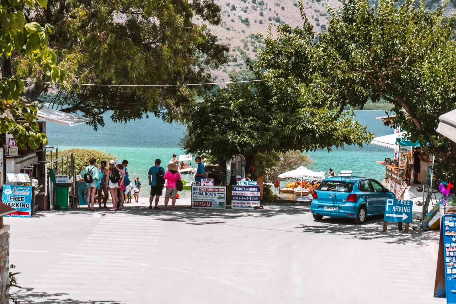 Accès au lac Kournas depuis le parking, entre arbres, boutiques et eau turquoise