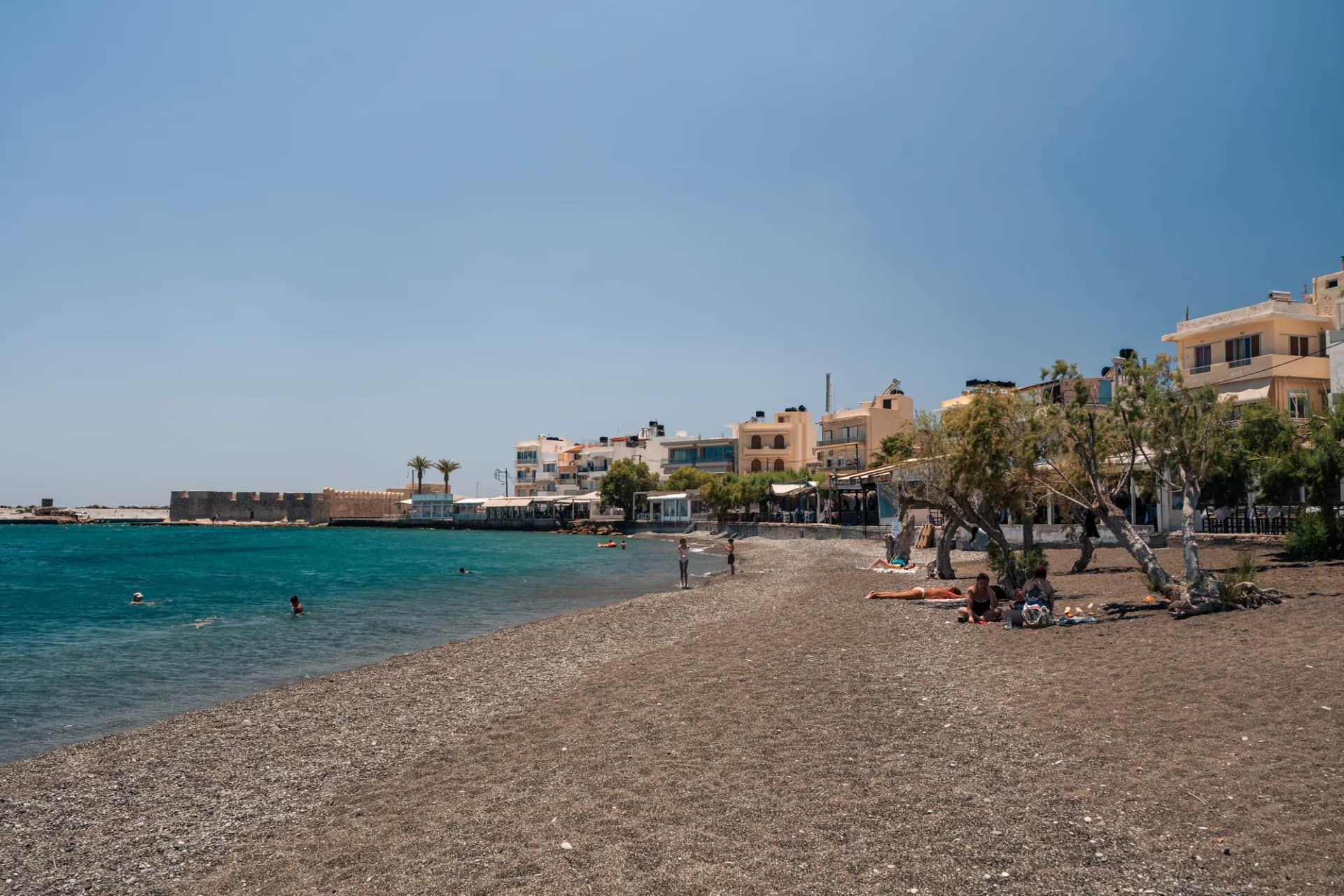 La plage de galets d'Ierapetra, ses tamaris et ses maisons, avec la forteresse Kales au bout de la baie