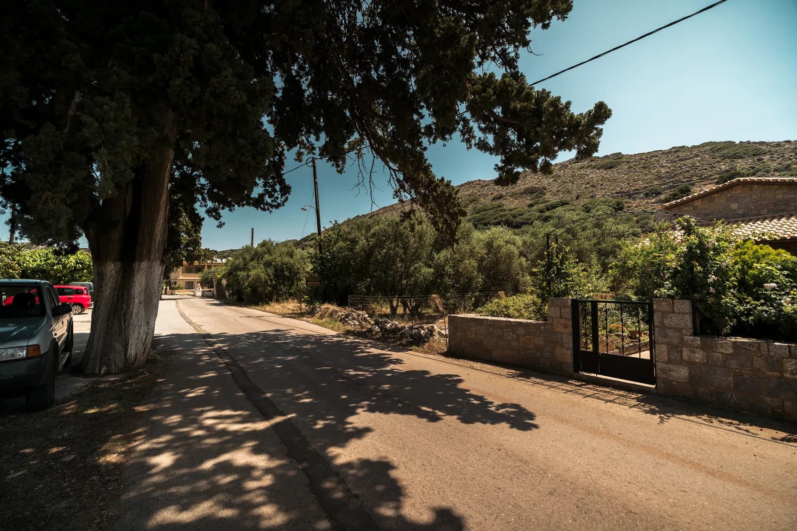 Route étroite bordée de murets et de voitures garées à l'entrée d'un village de l'est de la Crète