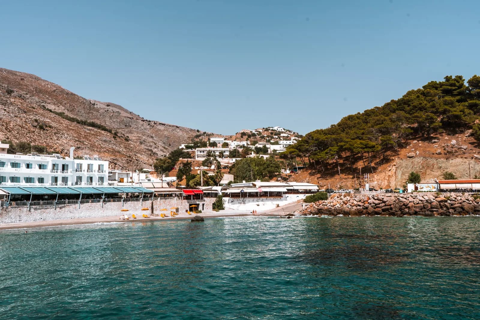 Maisons blanches et tavernes au bord d'une eau turquoise, au pied des montagnes de la côte de Sfakia