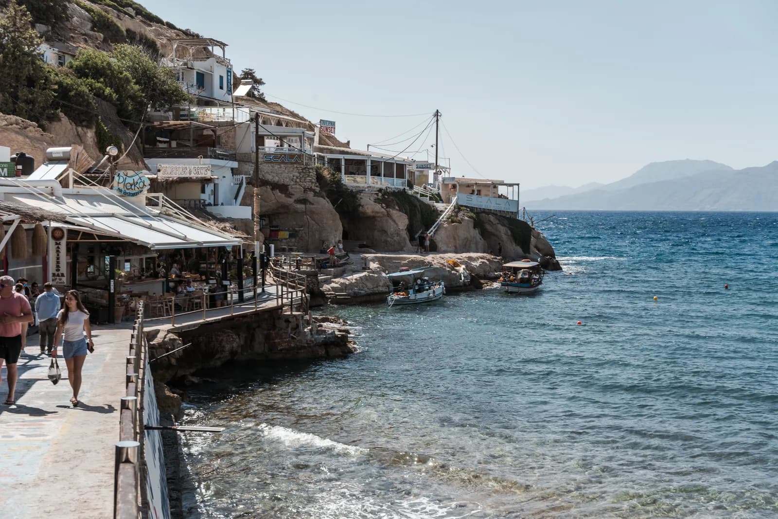 Le front de mer de Matala, ses tavernes accrochées aux rochers et la mer agitée face aux montagnes