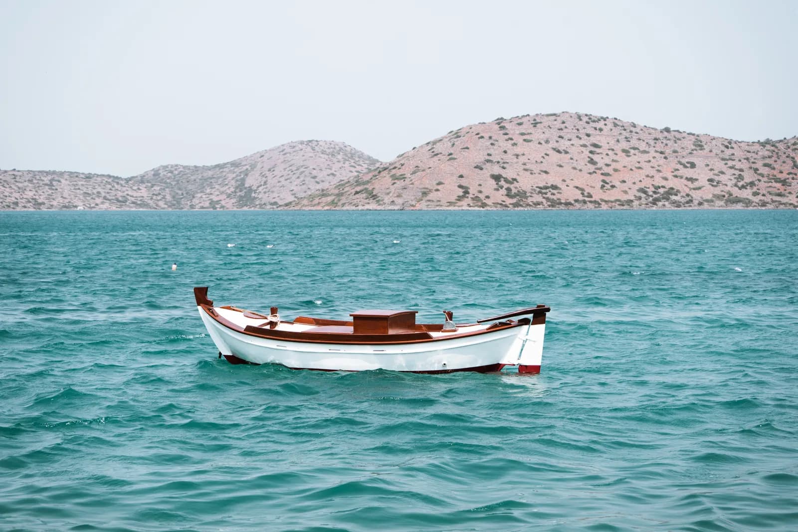 Barque de pêche traditionnelle sur l'eau turquoise du golfe d'Elounda, face aux collines