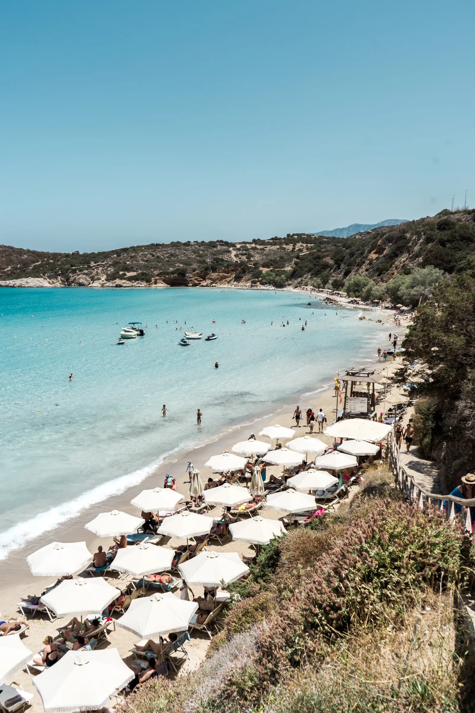 La plage de Voulisma, ses rangées de parasols blancs et son eau turquoise vues du sentier