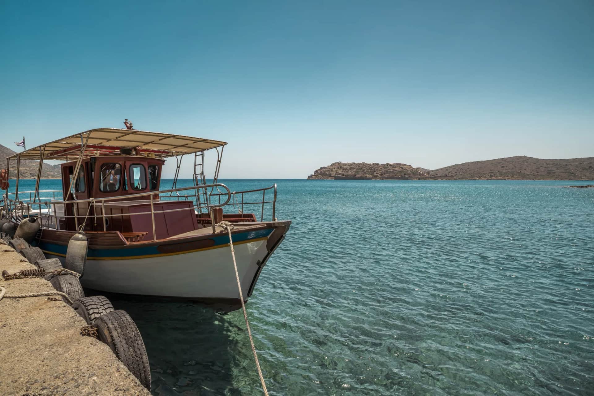 Caïque amarré au quai de Plaka dans une eau limpide, face à l'île de Spinalonga de l'autre côté du détroit