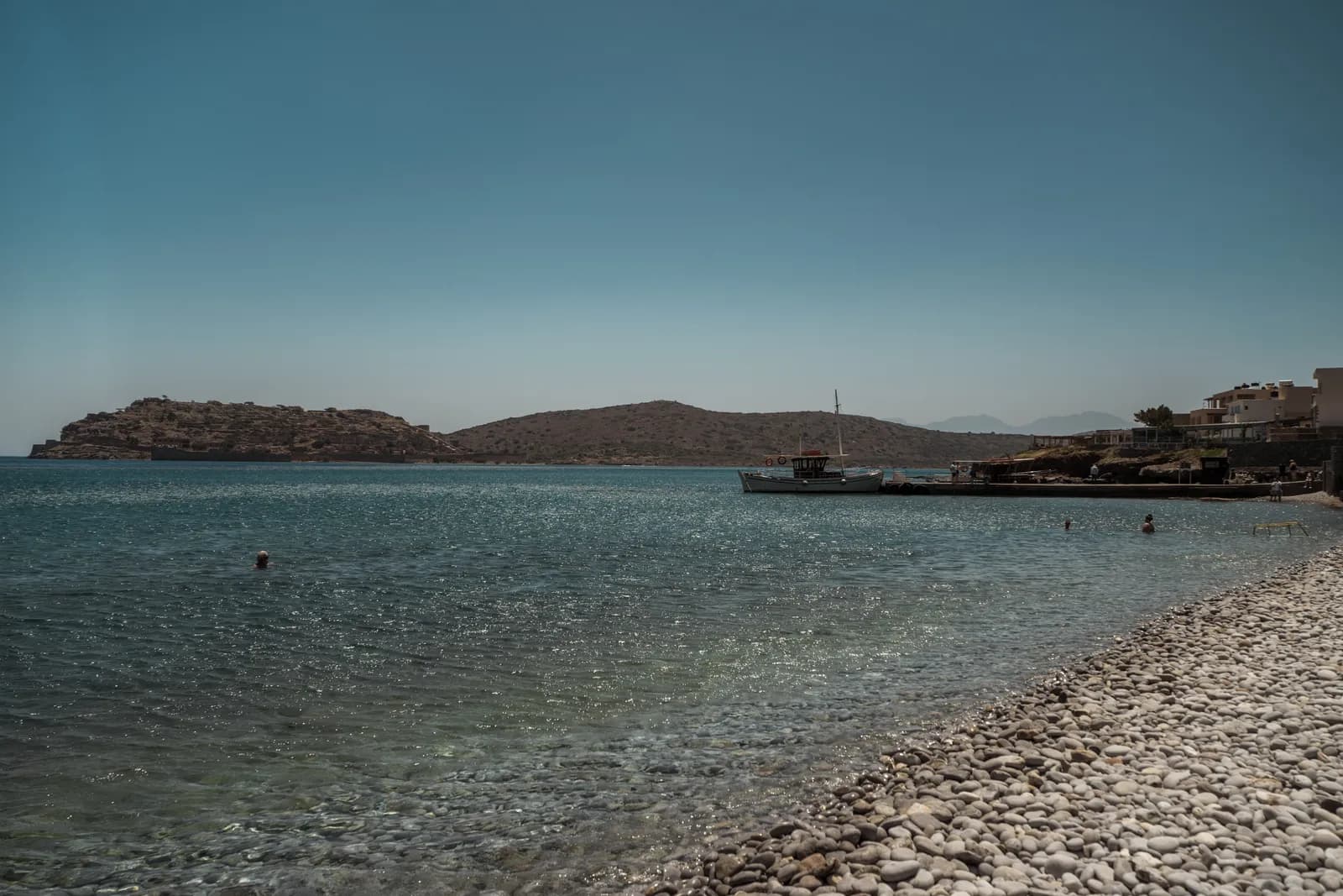 La plage de galets blancs de Plaka et son eau transparente, avec l'île de Spinalonga en face