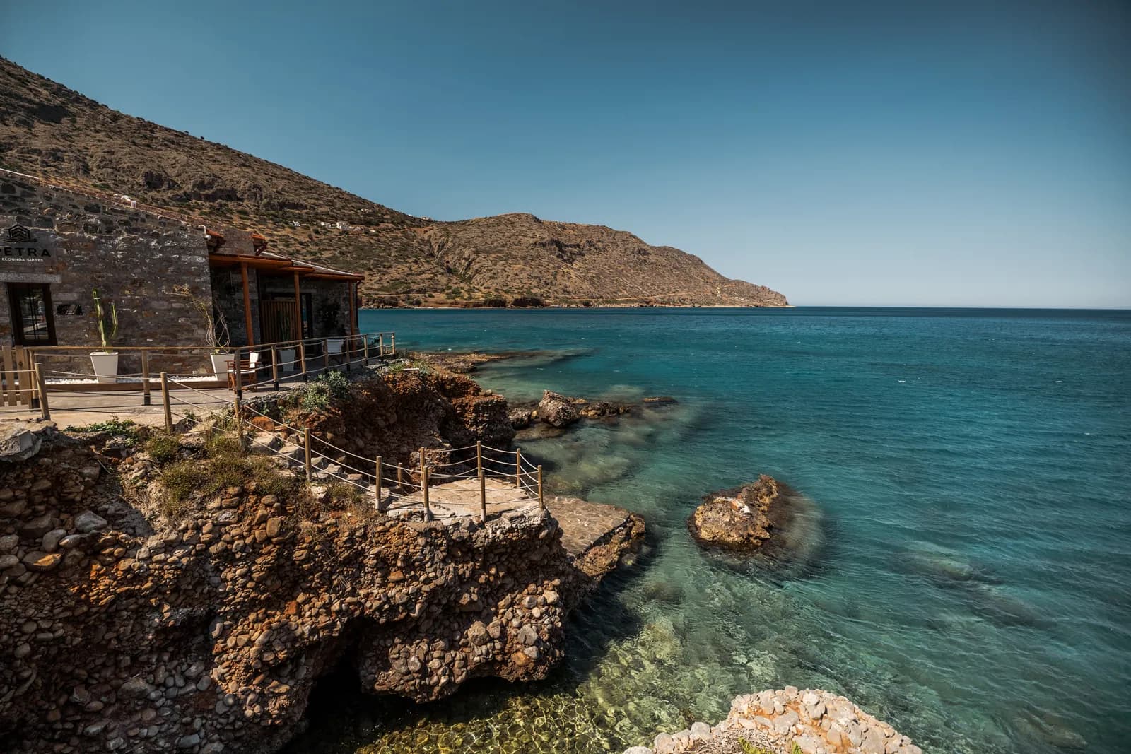 Côte rocheuse et eau turquoise près de Plaka, avec une terrasse en bois au bord de la mer