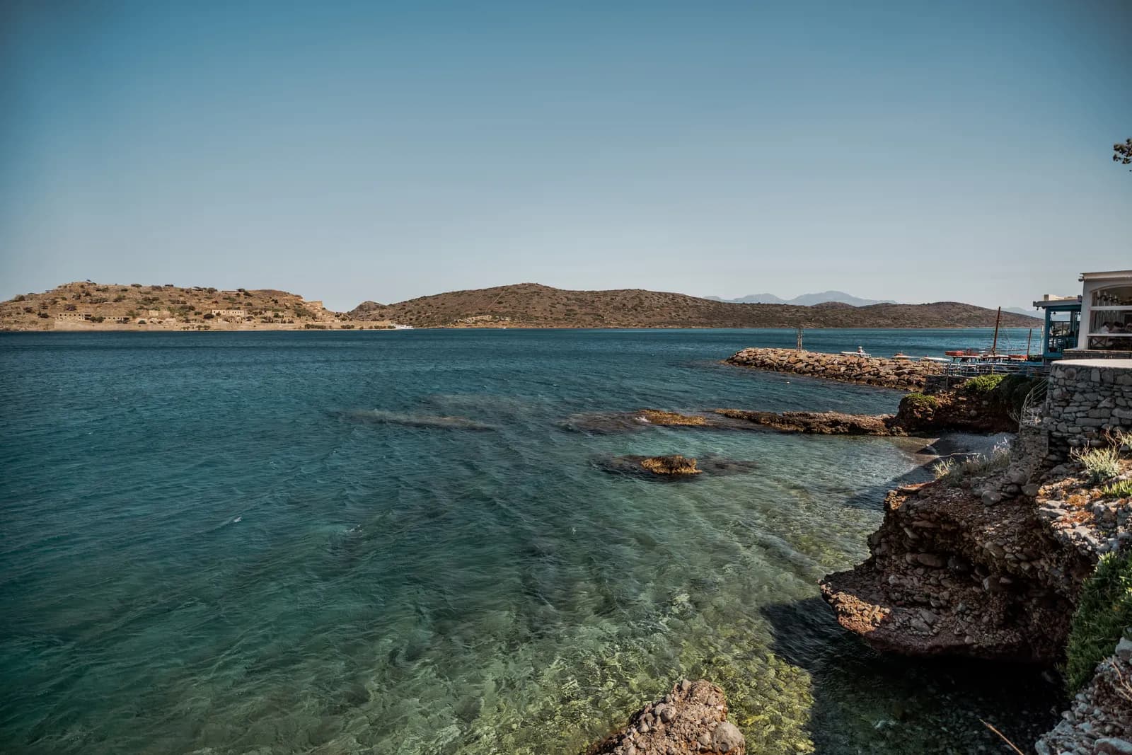 L'îlot de Spinalonga vu depuis la côte rocheuse de Plaka, au-dessus d'une eau transparente