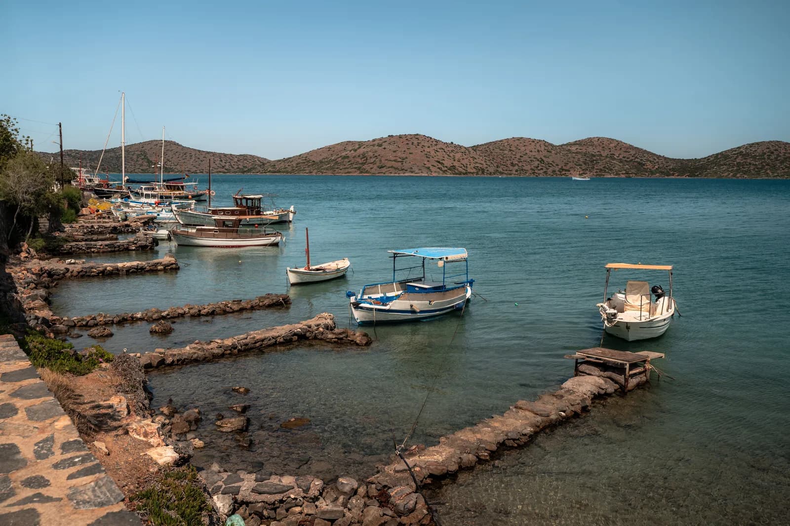 Barques amarrées à de petites jetées de pierre sur la rive du golfe d'Elounda, face aux collines