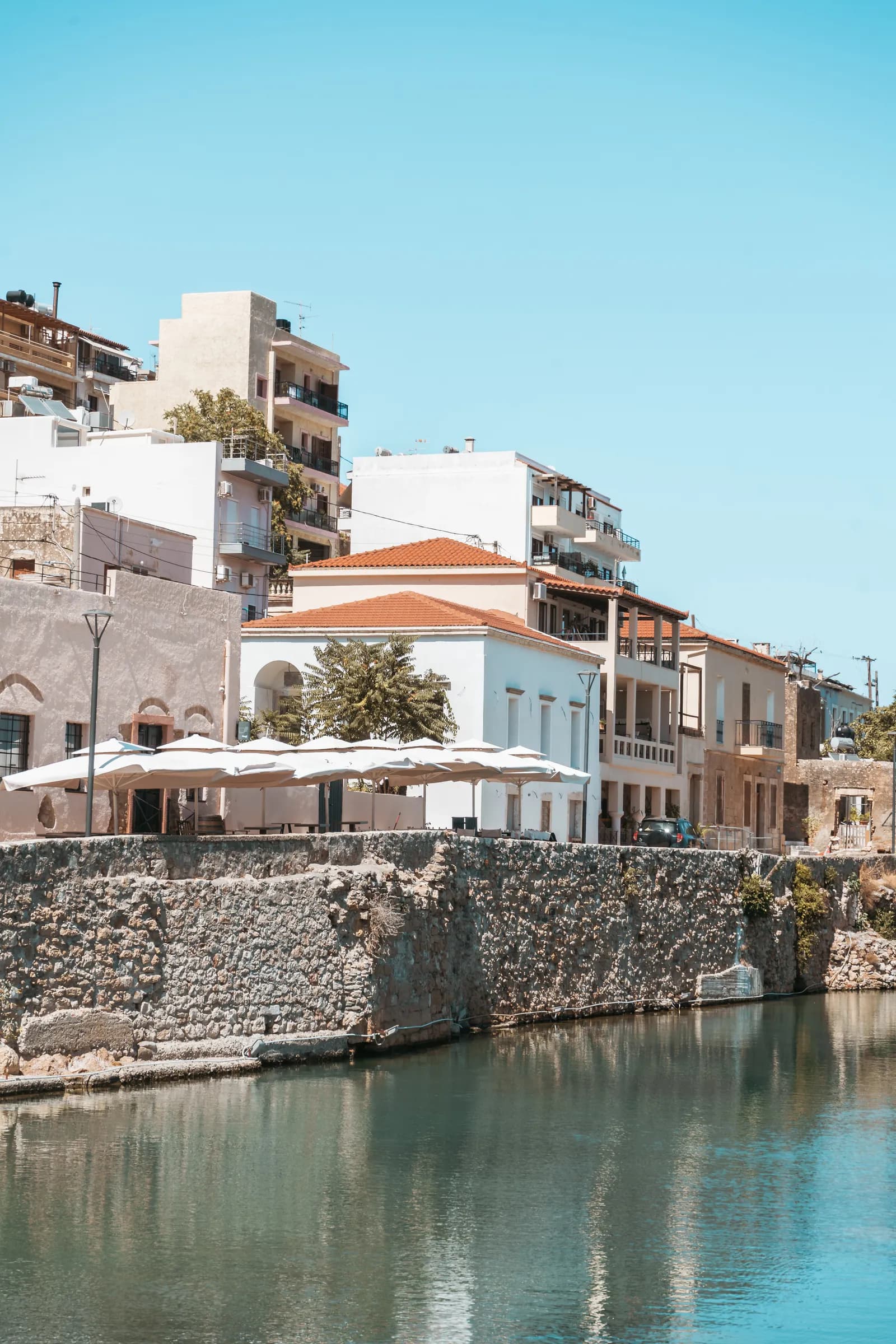 Maisons aux toits de tuiles et terrasse ombragée au-dessus d'un vieux quai de pierre sur le port de Sitia