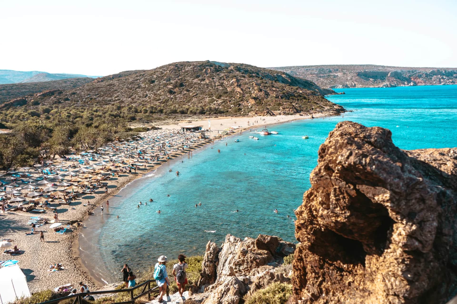 La baie de Vai vue des rochers, sa plage bordée de parasols et son eau turquoise au pied de la colline