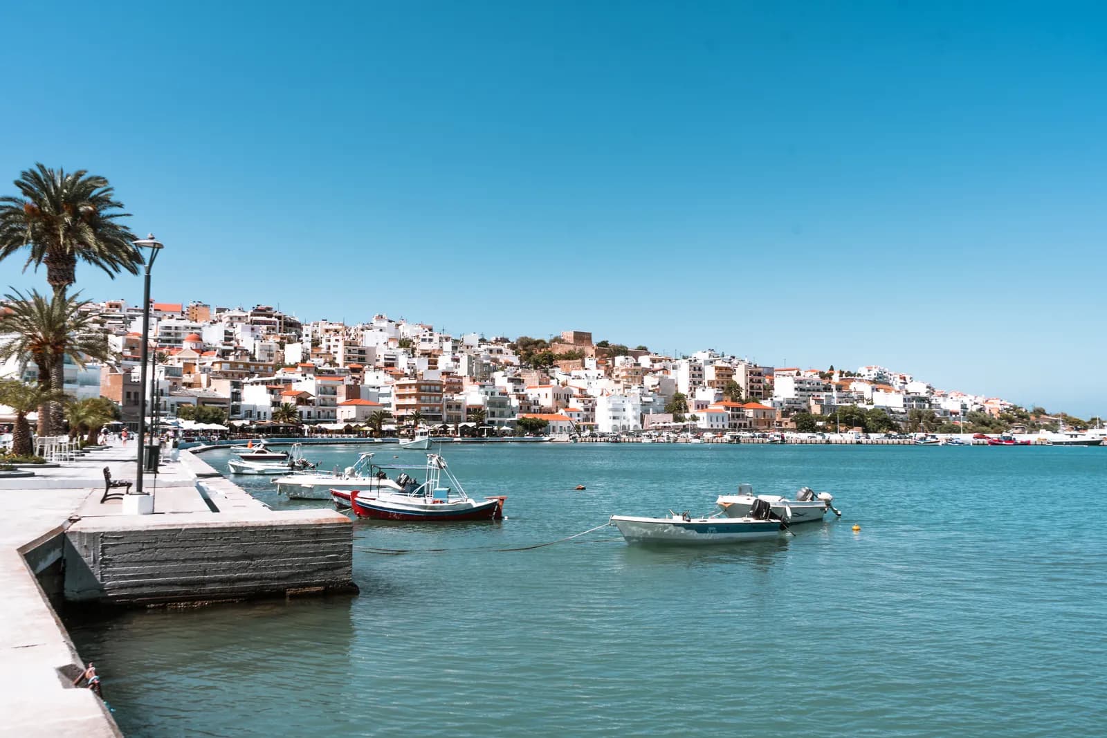 Le front de mer de Sitia, ses palmiers et ses barques devant la ville blanche étagée sur la colline