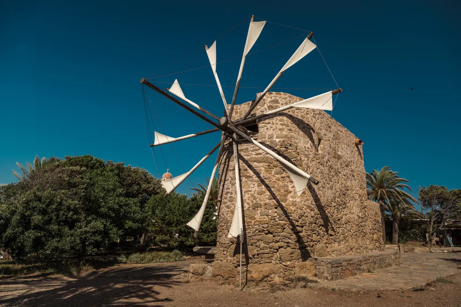 Moulin à vent en pierre aux ailes de toile blanche sous un ciel bleu profond, près du monastère de Toplou