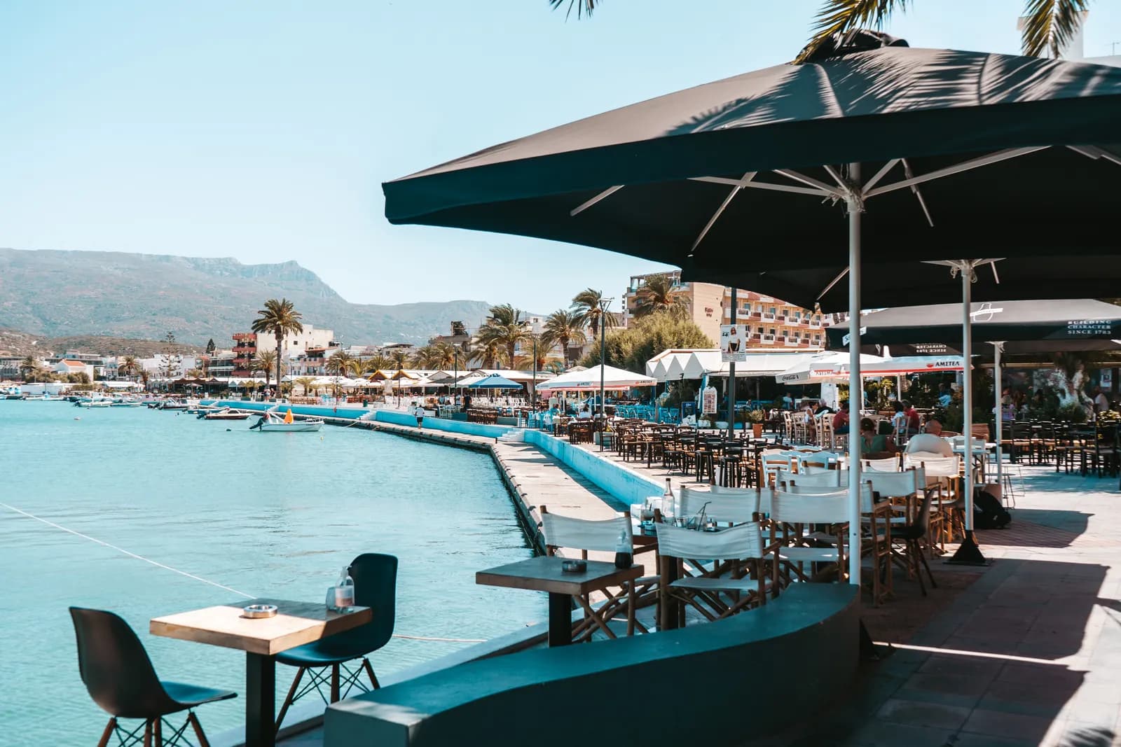 Terrasses de cafés sous les parasols le long du front de mer de Sitia, les montagnes en arrière-plan