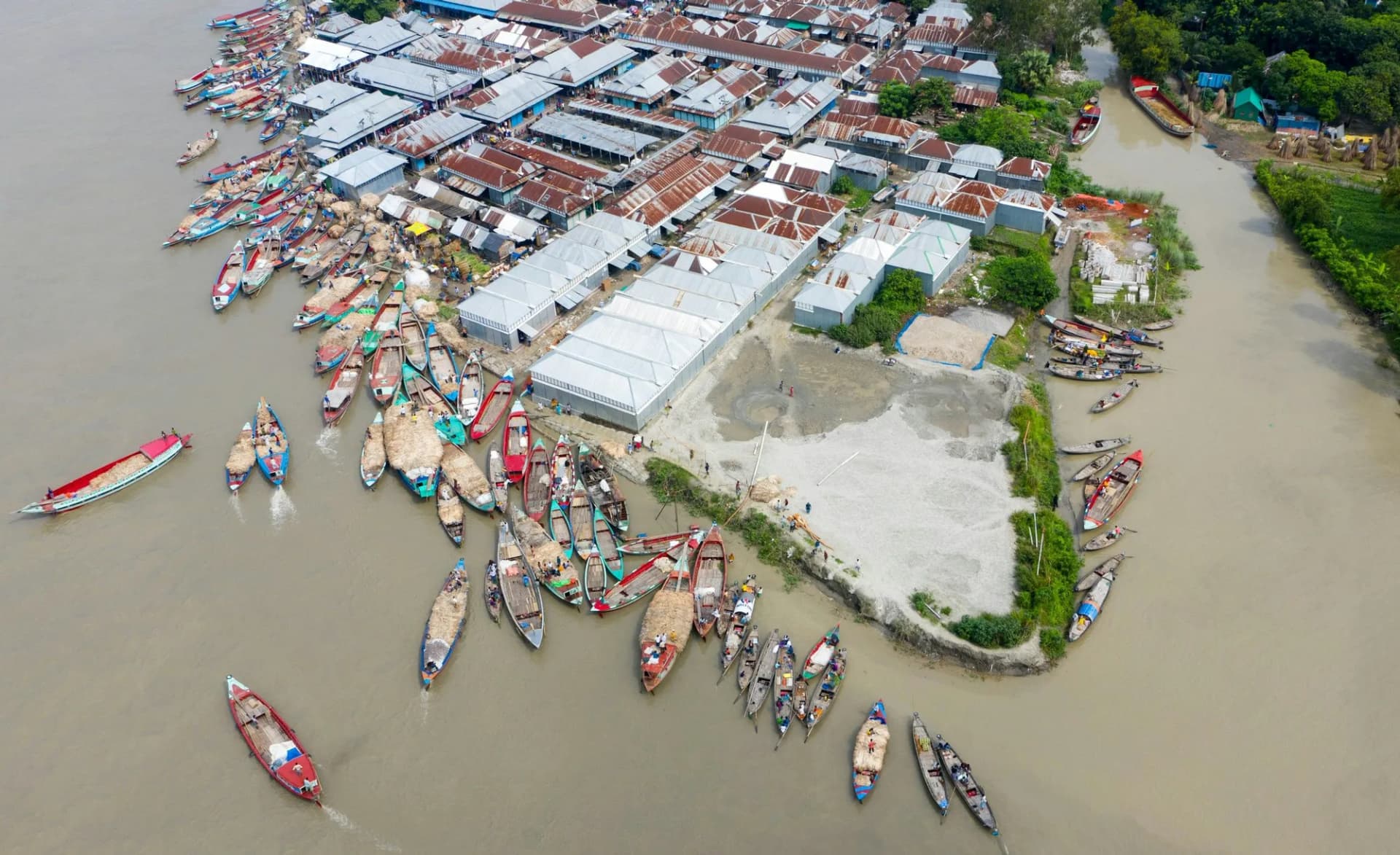 Vue aérienne de dizaines de bateaux en bois colorés chargés de jute amarrés au bord d'une rivière au Bangladesh