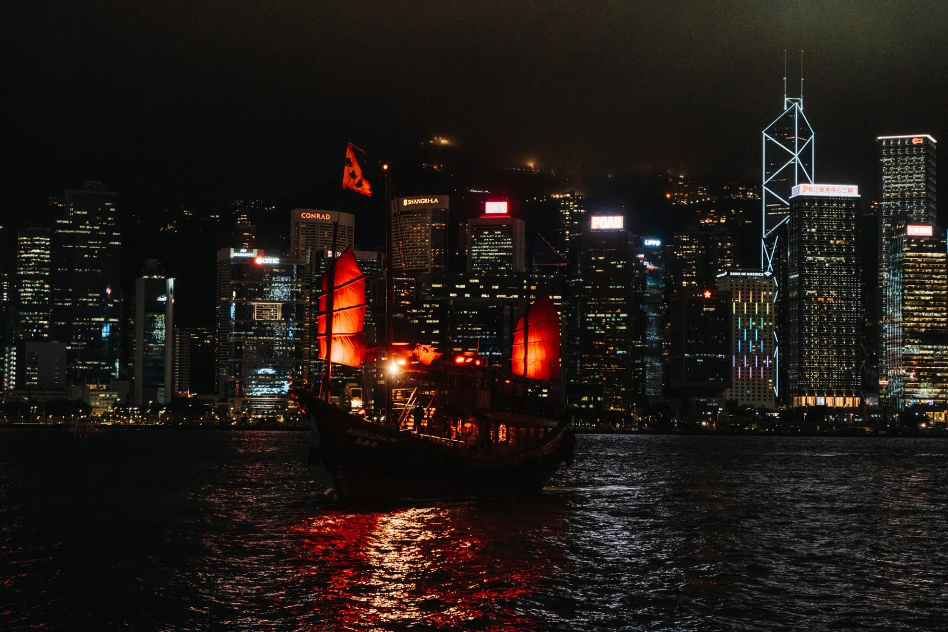 Jonque aux voiles rouges sur le port Victoria devant les gratte-ciel illuminés de Central, à Hong Kong, la nuit