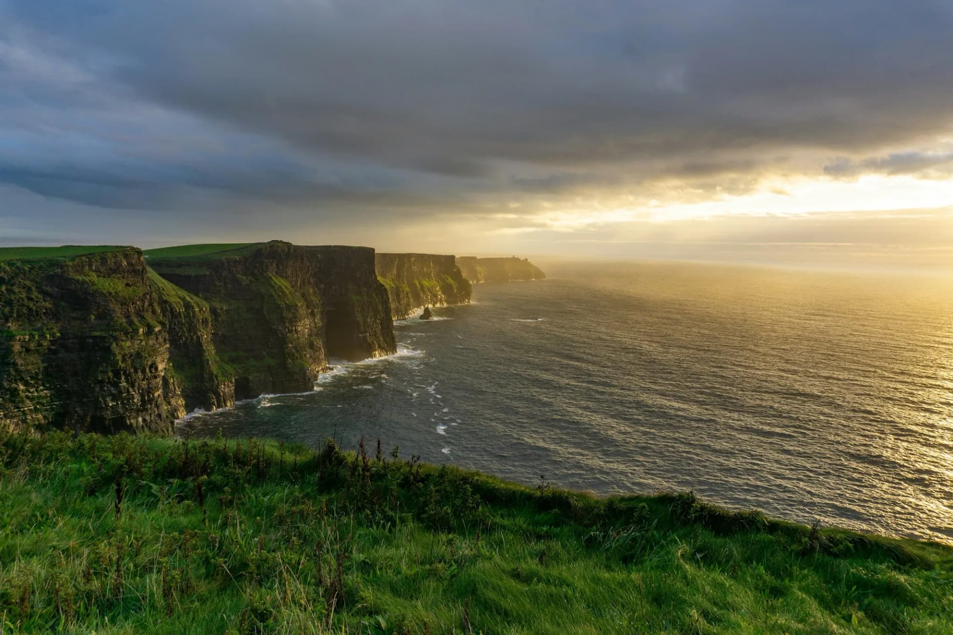 Falaises de Moher baignées d'une lumière dorée au-dessus de l'Atlantique, sous un ciel chargé de nuages