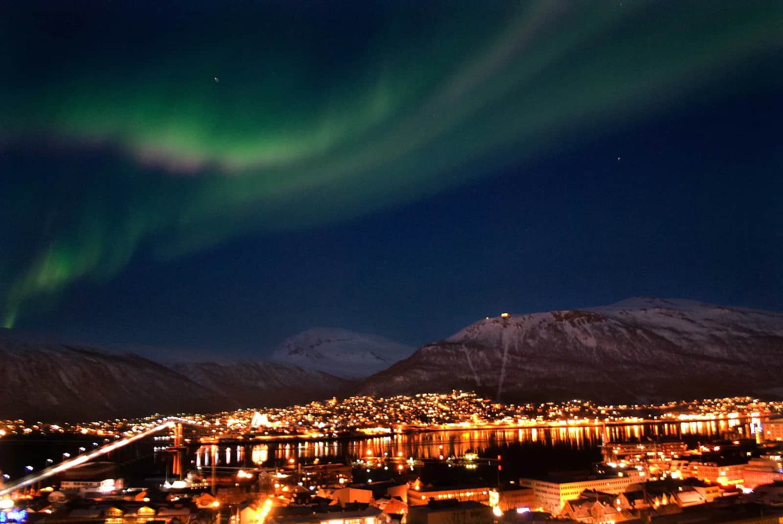 Aurore boréale verte au-dessus des lumières de Tromsø, de son pont et des montagnes enneigées, en janvier