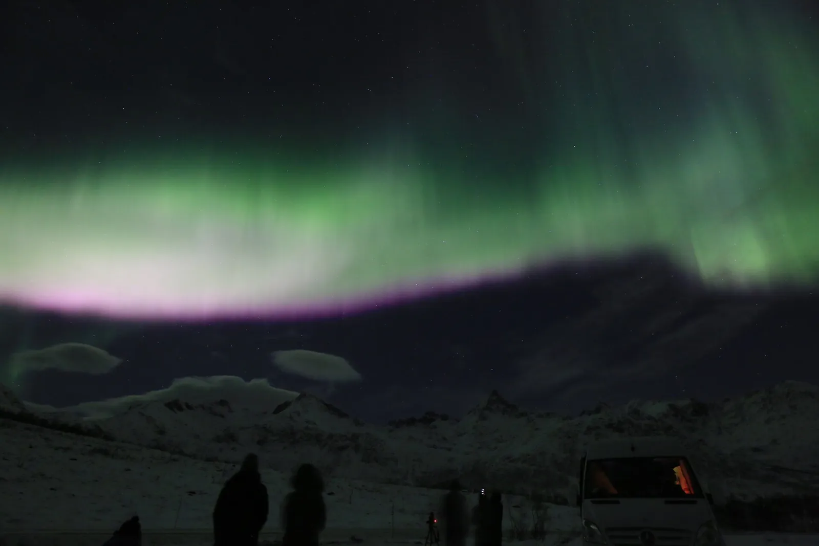 Aurore boréale au-dessus des montagnes près de Tromsø, observée par un petit groupe en excursion à côté de son minibus