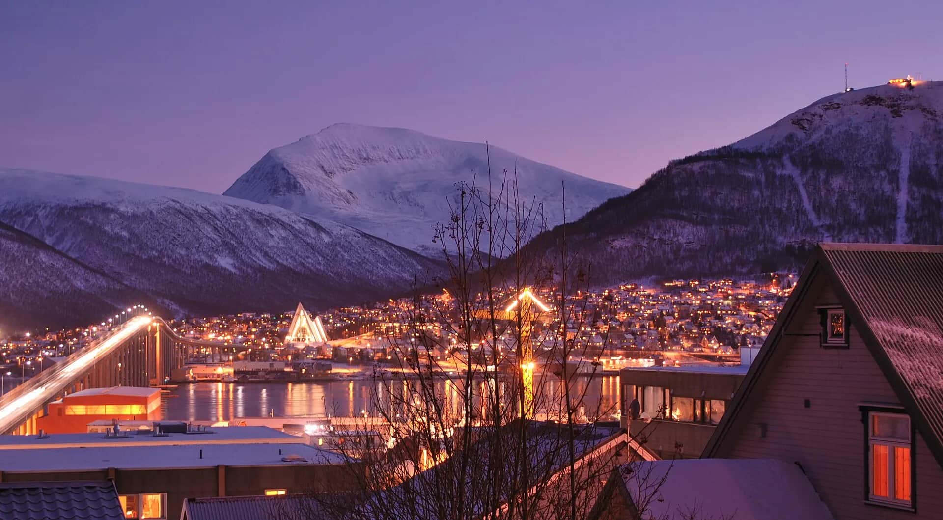 Tromsø en début d'après-midi pendant la nuit polaire, avec le pont, la cathédrale arctique illuminée et les montagnes enneigées