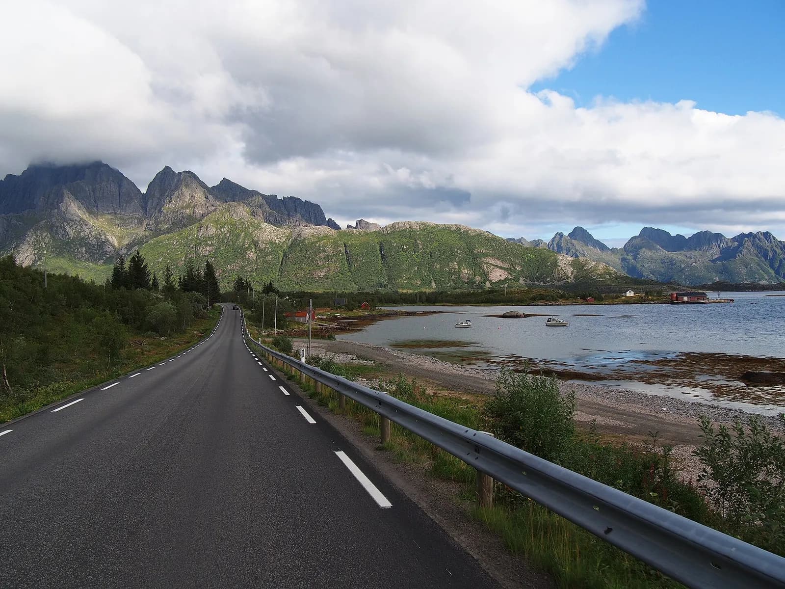 La route E10 au bord d'un fjord des Lofoten, au pied de sommets découpés, en août