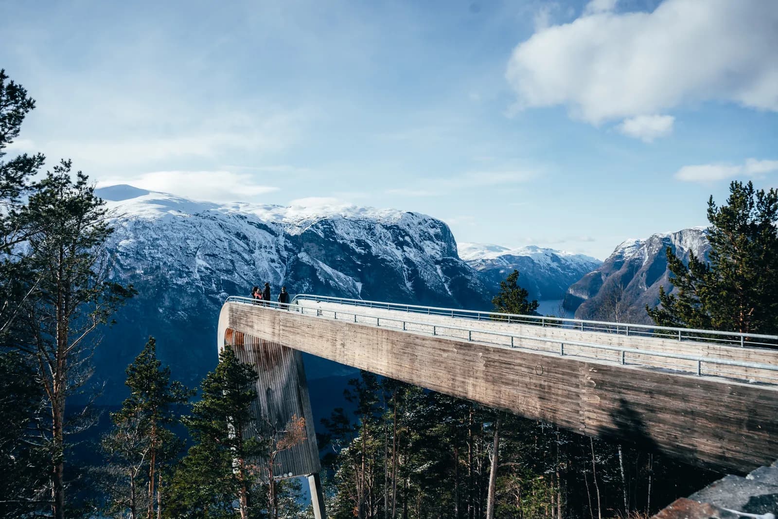 Visiteurs au bout de la passerelle de Stegastein, face aux montagnes enneigées, le 26 mars 2023