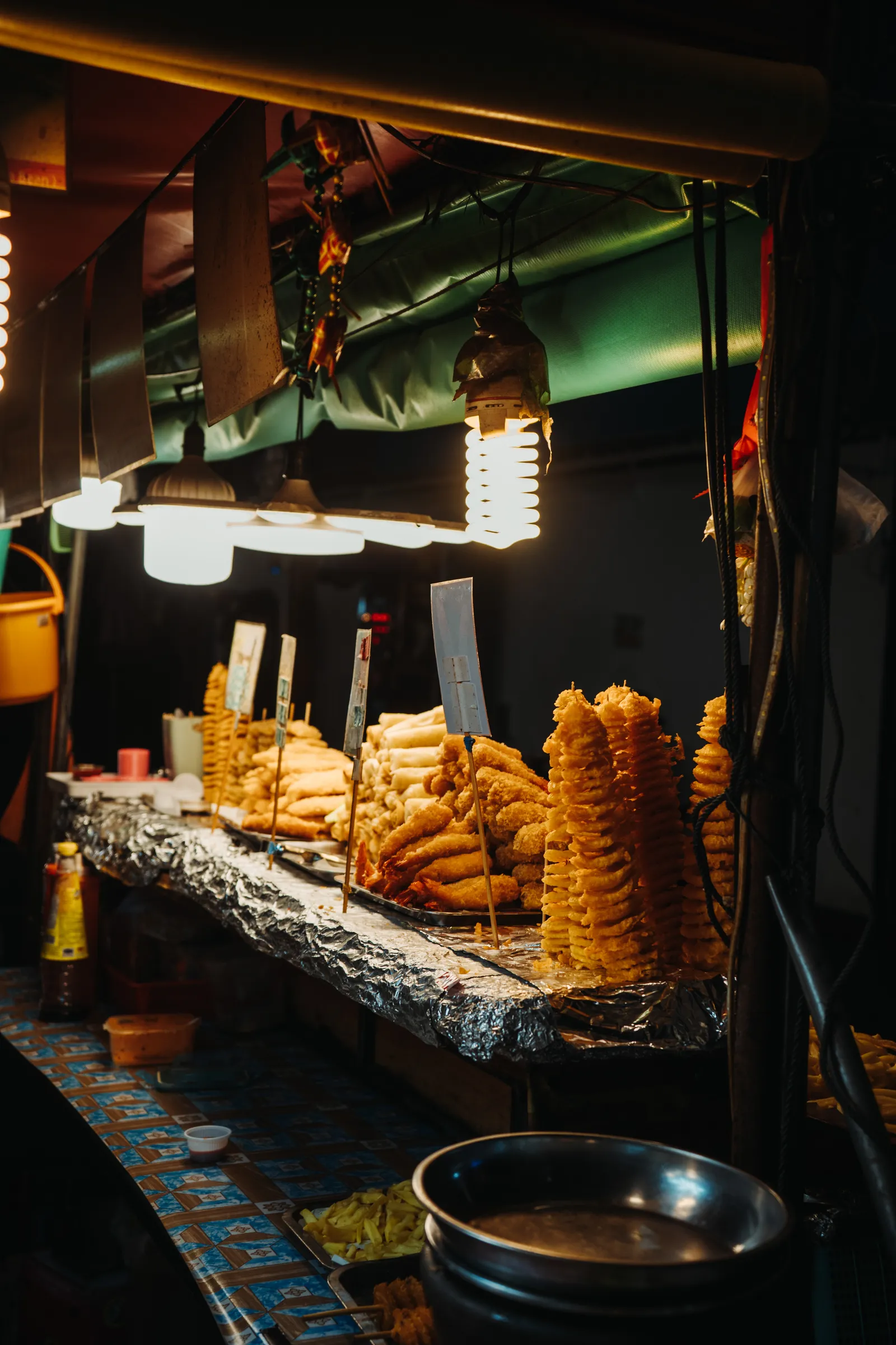 Stand de pommes de terre en spirale et de beignets sous les ampoules d'un marché de nuit de Patong