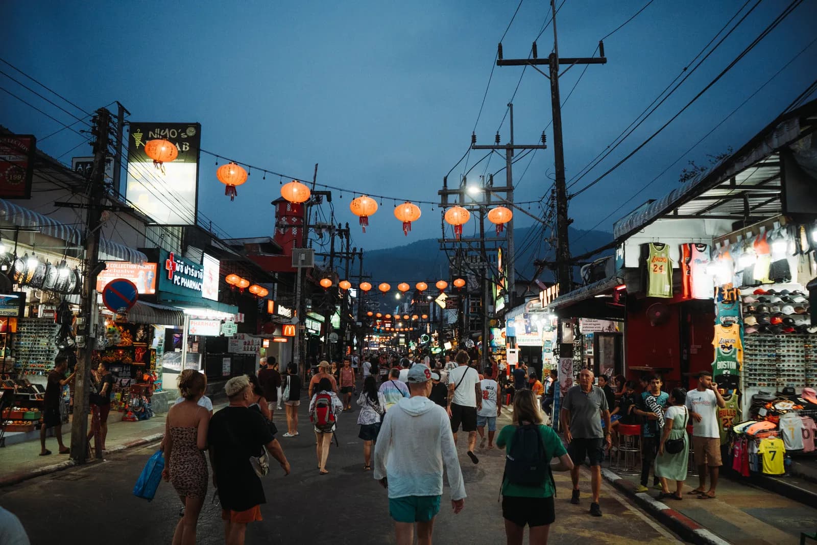 Flot de touristes sous les lanternes rouges de Bangla Road à l'heure bleue, boutiques de maillots éclairées