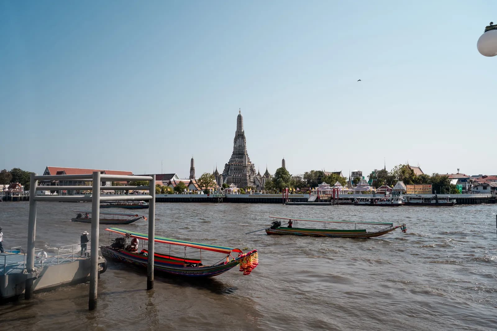 Wat Arun vu depuis la rive de la Chao Phraya, avec un bateau long-tail au premier plan, à Bangkok