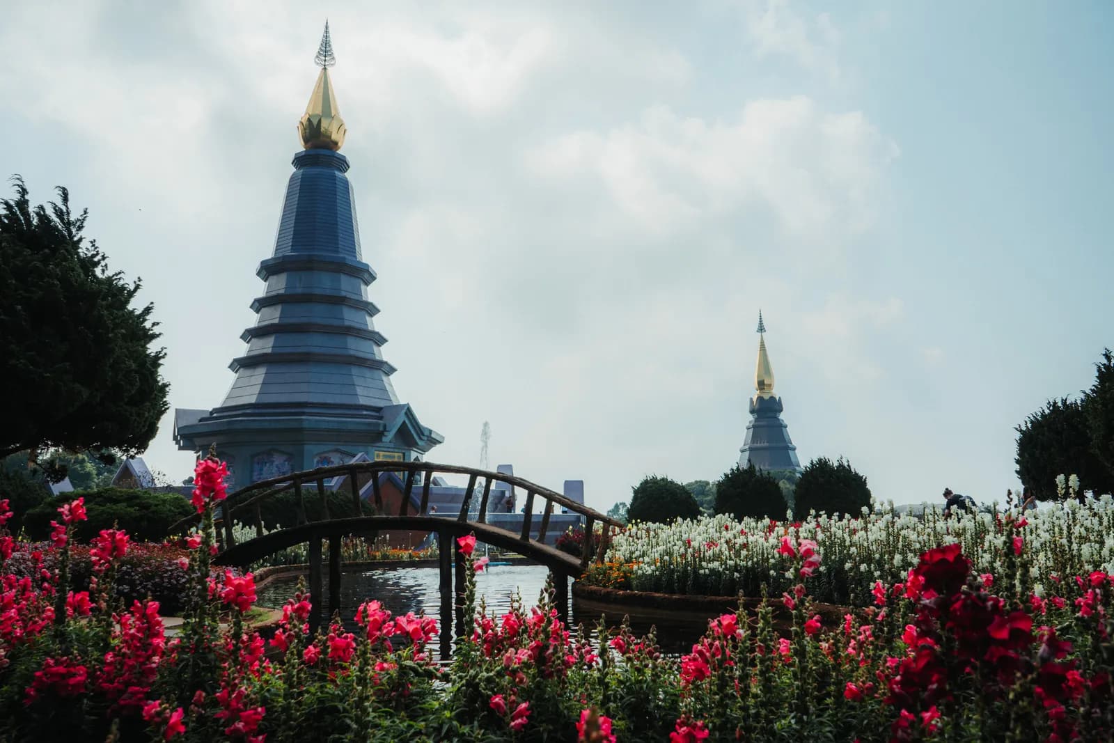 Les deux chedis royaux du Doi Inthanon derrière un pont en arc et des massifs de fleurs rouges