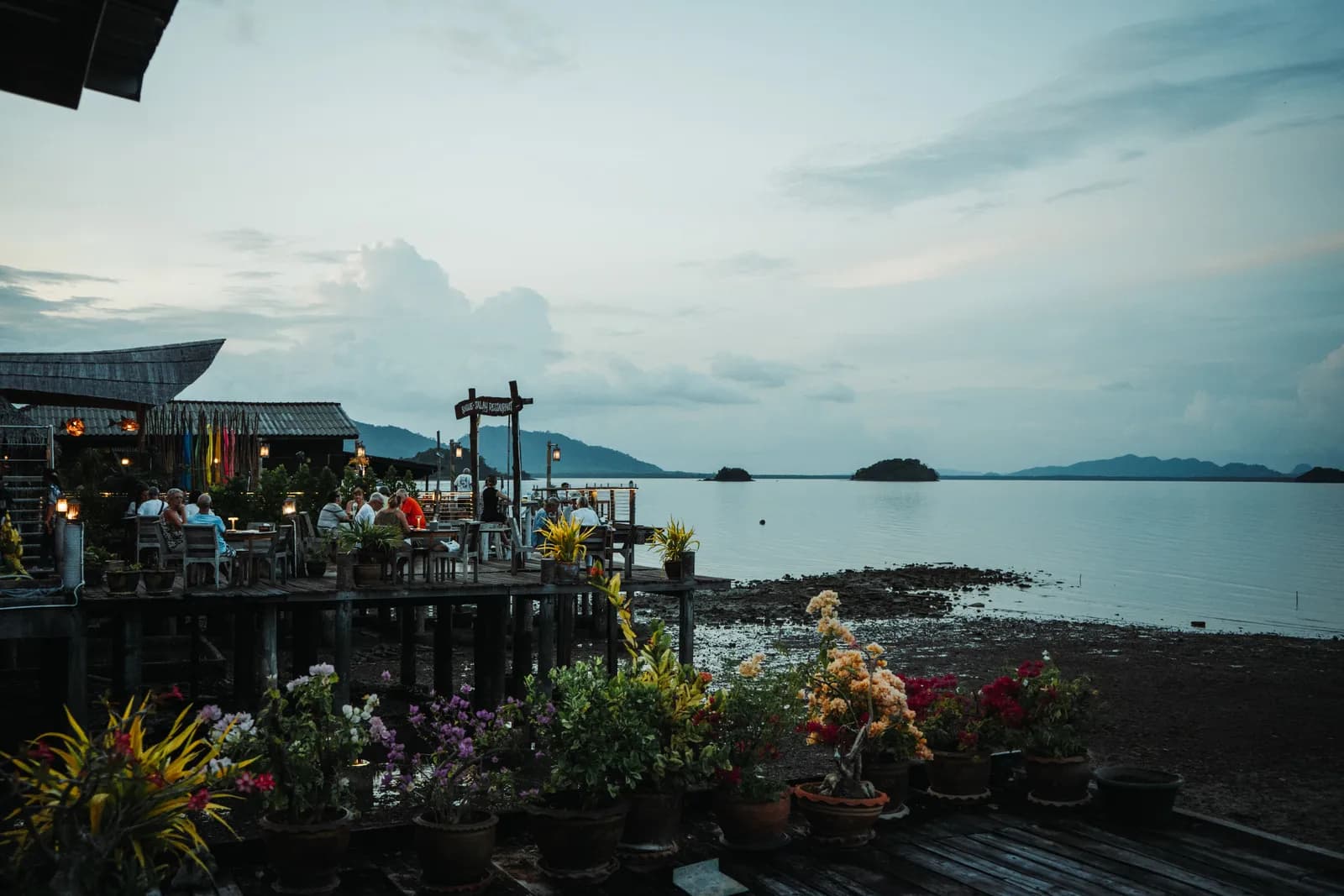 Restaurant sur pilotis fleuri de la vieille ville de Koh Lanta, avec des îles à l'horizon au crépuscule