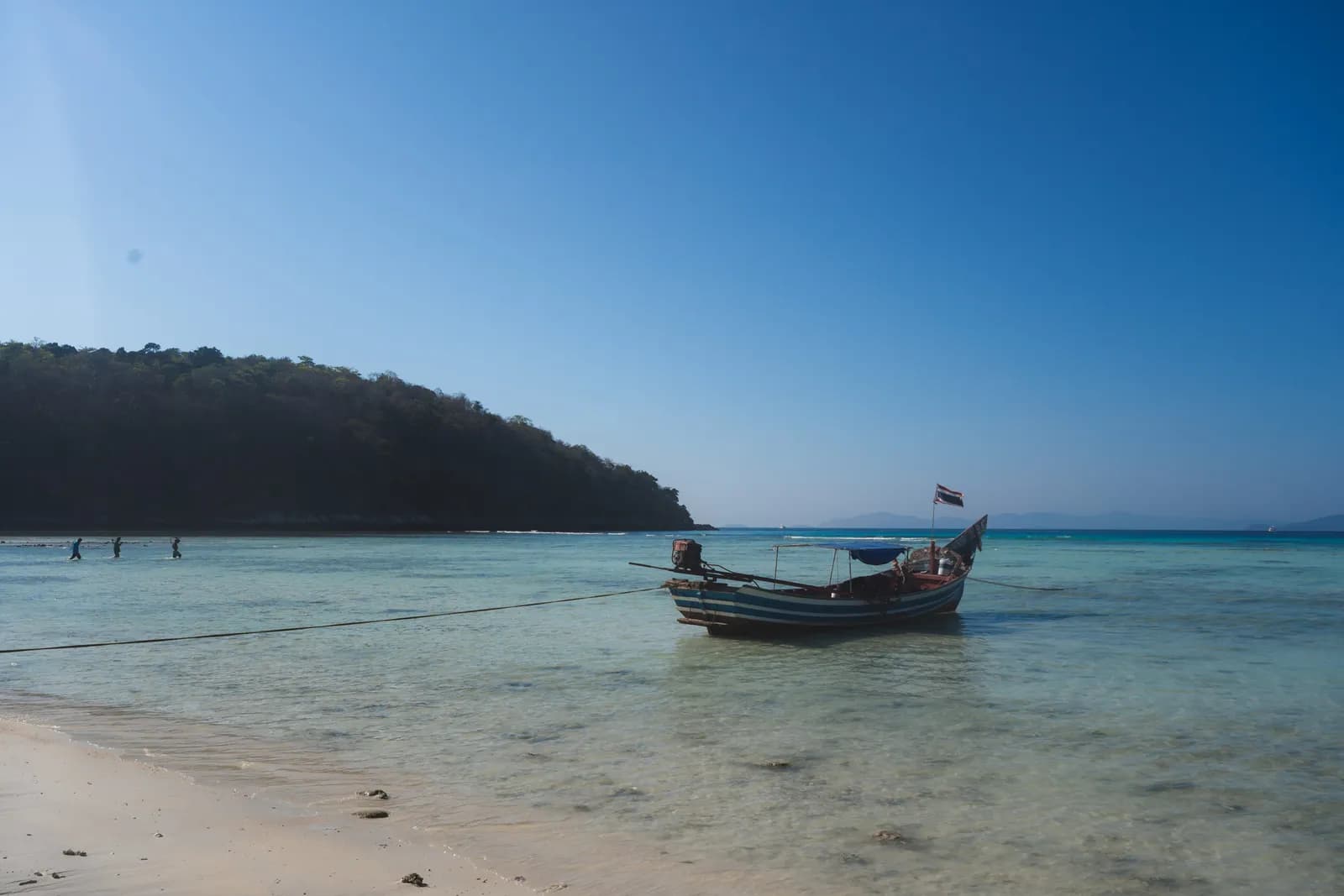 Bateau long-tail amarré dans l'eau claire de la baie principale de Koh Racha Yai, colline boisée en face