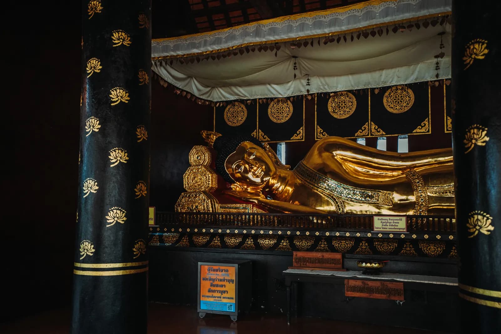 Bouddha couché doré entre des colonnes noires semées de lotus dans le pavillon de Wat Chedi Luang