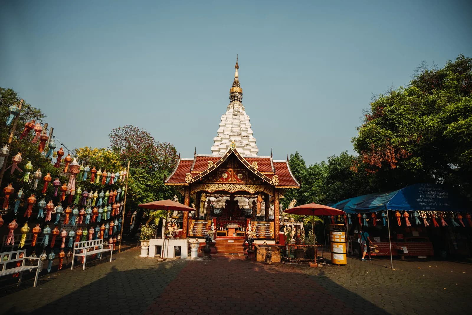 Rideau de lanternes lanna colorées devant le chedi blanc et le pavillon doré de Wat Muen Tum, à Chiang Mai