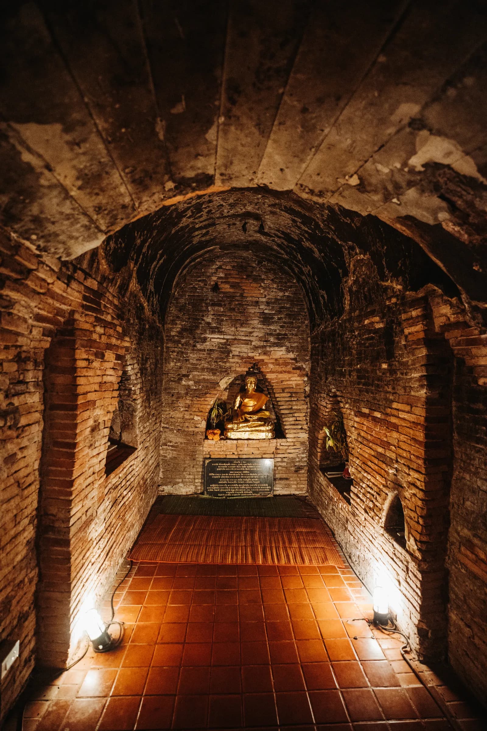 Tunnel voûté en briques de Wat Umong menant à une niche où brille un Bouddha doré