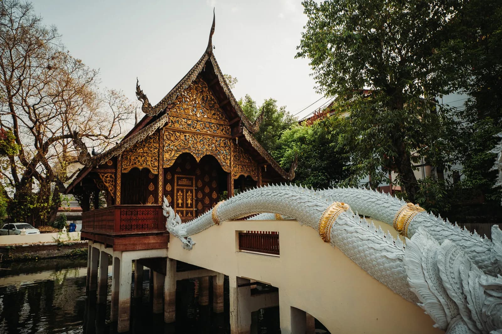 Bibliothèque en bois sculpté sur pilotis au-dessus d'un bassin, avec un naga blanc, à Wat Chiang Man