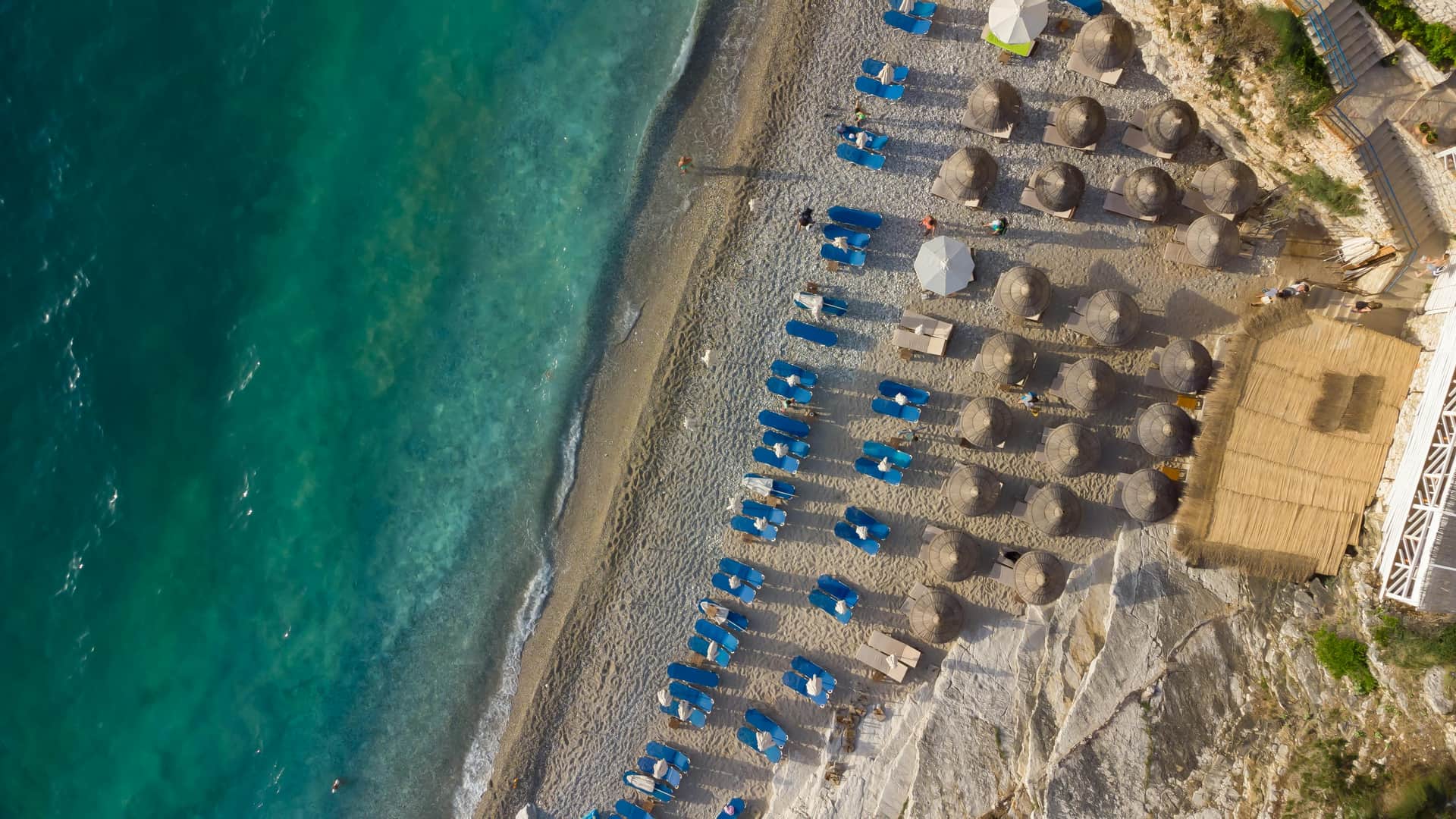 Plage de sable noir volcanique à Santorin avec mer bleu azur et falaises en arrière-plan