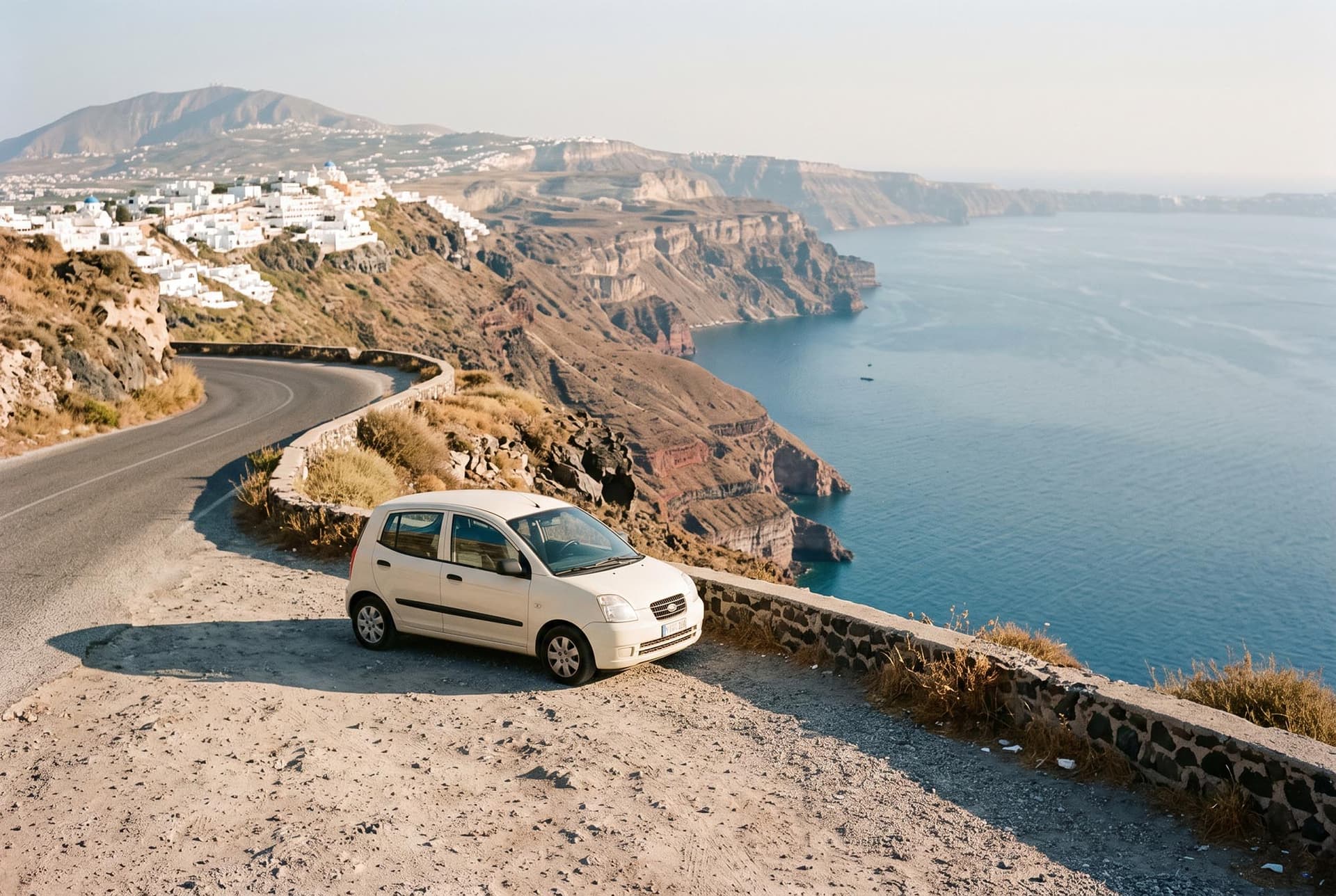 A small city car parked on a balcony road above the Santorini caldera