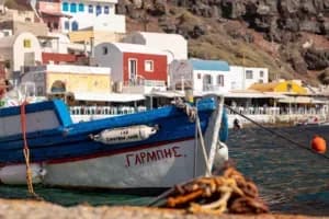 Le port d'Ammoudi Bay avec ses bateaux de pêche et falaises rouges