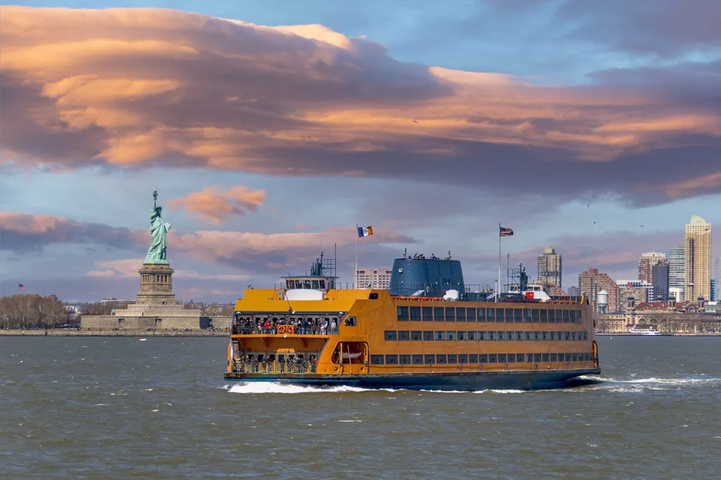 Ferry de Staten Island venant de Manhattan et passant par la Statue de la Liberté. La Statue de la Liberté et les gratte-ciel du bas de Manhattan sont visibles en arrière-plan.